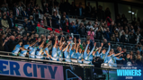 Football team celebrating winning the Carabao Cup, 2026, with crowd applauding. Players are holding a trophy on a platform.