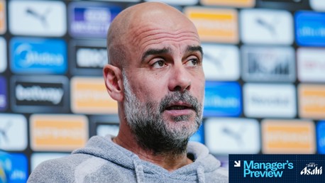 A person in a grey hoodie at a press conference with a background of sponsor logos. The image features a 'Manager's Preview' graphic with the Asahi logo.