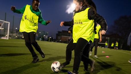 Young players participate in a football game at dusk, wearing bright yellow bibs on an artificial turf field.