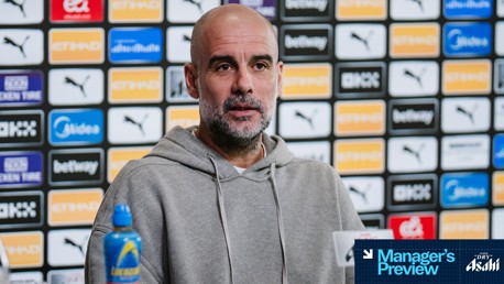 A person in a grey hoodie at a press conference with a blurred face. Background features Manchester City logos and sponsorships including Puma and Etihad.