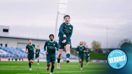 Football players in Manchester City training kits running on a field with a badge indicating 'Official Verdict' in the bottom right corner.