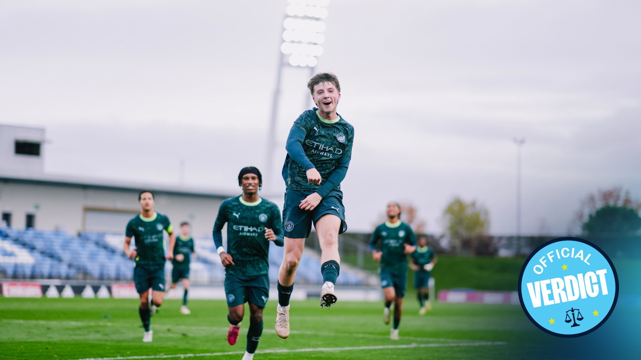 Football players in Manchester City training kits running on a field with a badge indicating 'Official Verdict' in the bottom right corner.