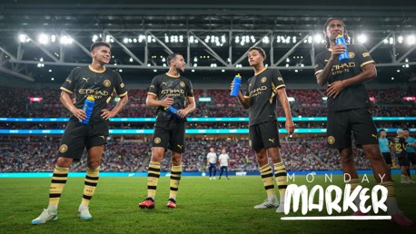 Four Manchester City football players in black and gold kits are holding blue water bottles on a football field, with stadium lights and crowd in the background. Text reads 'Monday Marker'.