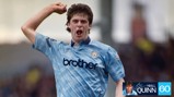 A football player in a vintage Manchester City kit celebrates with a clenched fist. The shirt features 'brother' as the sponsor and the Manchester City crest on the chest.