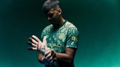 A person wearing a Manchester City goalkeeper kit, adjusting their gloves. The shirt has hexagonal patterns and the Manchester City crest is visible.