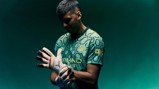 A person wearing a Manchester City goalkeeper kit, adjusting their gloves. The shirt has hexagonal patterns and the Manchester City crest is visible.