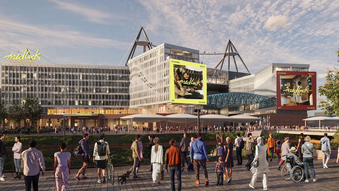The image features the Medlock Hotel with a modern architectural design. The facade displays the hotel's branding prominently. There is a crowd of people, some with pets, walking in front of the building under a clear sky.