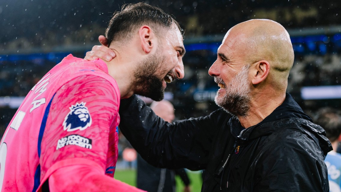 A football coach in a raincoat grasps a Premier League player in a pink jersey labeled 'No room for racism,' engaging in conversation, likely after a match.