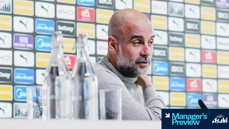 A Manchester City press conference setting with a blurred individual in the foreground. The background displays a variety of sponsor logos. The image includes a label 'Manager's Preview'.