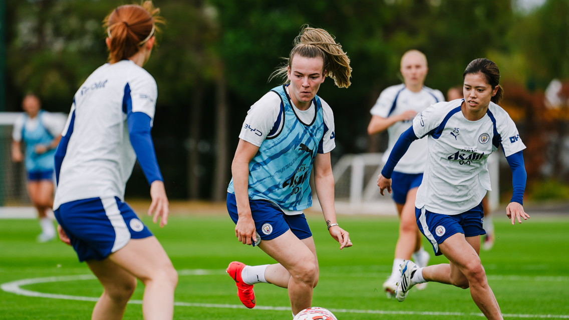 Female football players in white Manchester City training gear practicing on a field.