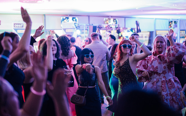 A lively party scene with people dancing under colorful lights in a crowded room.