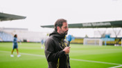 A person holding a microphone at a football stadium, dressed in Borussia Dortmund attire. The stadium is partially visible in the background.