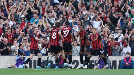 Football team players in red and black kits celebrate in front of cheering crowd.