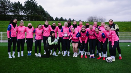 A group photo of the Manchester City women's team wearing pink training gear on a soccer field.
