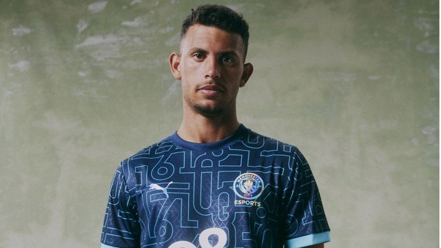 A person wearing a Manchester City eSports jersey by Puma, standing against a green background.