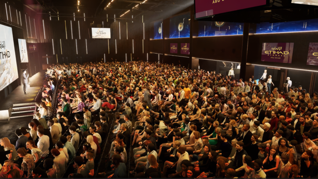 A large audience seated in a hall with Etihad Airways branding on screens. The stage features a presenter in front of the crowd.