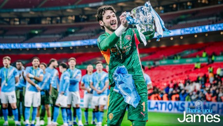 A Manchester City player holds a trophy while celebrating on the field, with teammates in the background. The words 'Thank you James' are visible at the bottom right.