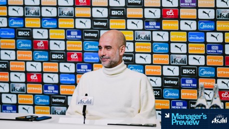 A person seated at a press conference table with a microphone, blurred face, and logo background featuring brands like Puma and Etihad Airways. Text overlay says 'Manager's Preview.'