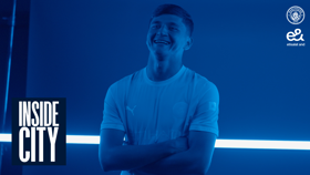 A person in a Manchester City shirt stands smiling with arms crossed in a blue-tinted image. The Manchester City logo and 'Inside City' text are visible.