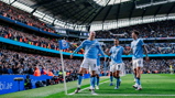 Manchester City players celebrating a goal at the Etihad Stadium with the crowd in the background.