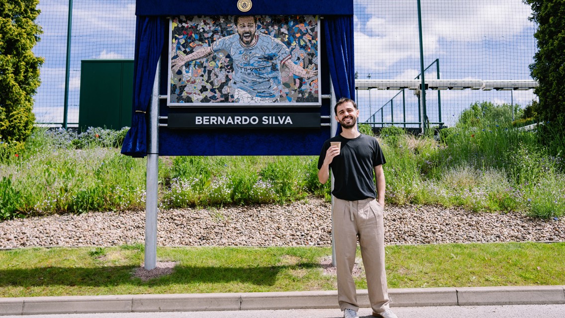 Person standing in front of a Bernardo Silva mosaic plaque and statue outdoors.
