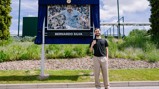 Person standing in front of a Bernardo Silva mosaic plaque and statue outdoors.