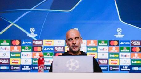 A blurred face is at a press conference setup with UEFA Champions League branding and sponsor logos. A Gatorade bottle is visible in the foreground.