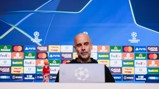 A blurred face is at a press conference setup with UEFA Champions League branding and sponsor logos. A Gatorade bottle is visible in the foreground.