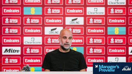 A press conference backdrop with Emirates FA Cup branding. The person in the image has their face blurred. Sponsor logos like Emirates, Carling, and ClearScore are visible. A microphone and a placard titled 'Manager's Preview' are in the foreground.