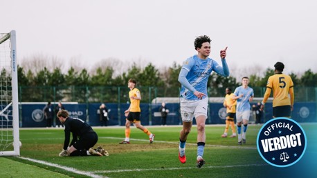 A soccer player in a Manchester City kit celebrates a goal on the field, while the opposing team's goalkeeper kneels near the goalpost.