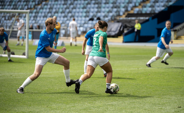 A soccer match in progress, featuring players in blue and green jerseys engaged in an active play on the field.