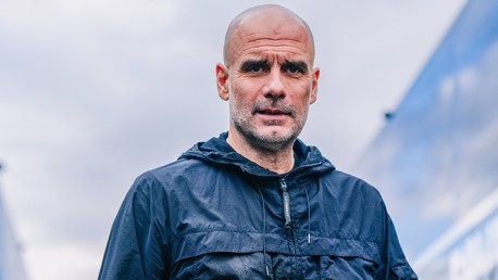 A person wearing a dark jacket stands outdoors against a cloudy sky.