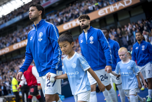Manchester City players walk hand in hand with young mascots at Etihad Stadium.