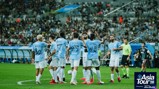 Manchester City players celebrating a goal during the Asia Tour '26, with branding for experience Abu Dhabi. The team is wearing light blue jerseys with logos and player names displayed in various languages.