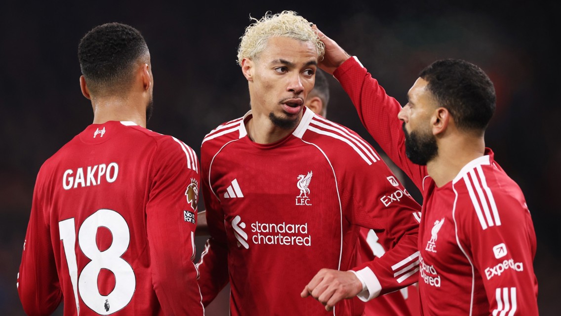 Liverpool players in red kits celebrate during a match. Gakpo with number 18 visible, standing with teammates.