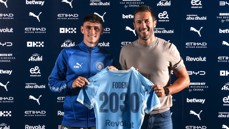 Two men holding a Manchester City jersey with 'Foden 2030' printed on the back, indicating a contract extension. Logos and sponsors visible in the background.