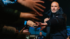 A man in a black jacket greets a crowd, reaching out to shake hands with multiple people.