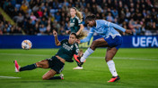 A soccer player in a Real Madrid jersey makes a tackle while a player in a Manchester City jersey takes a shot at the goal during a match.
