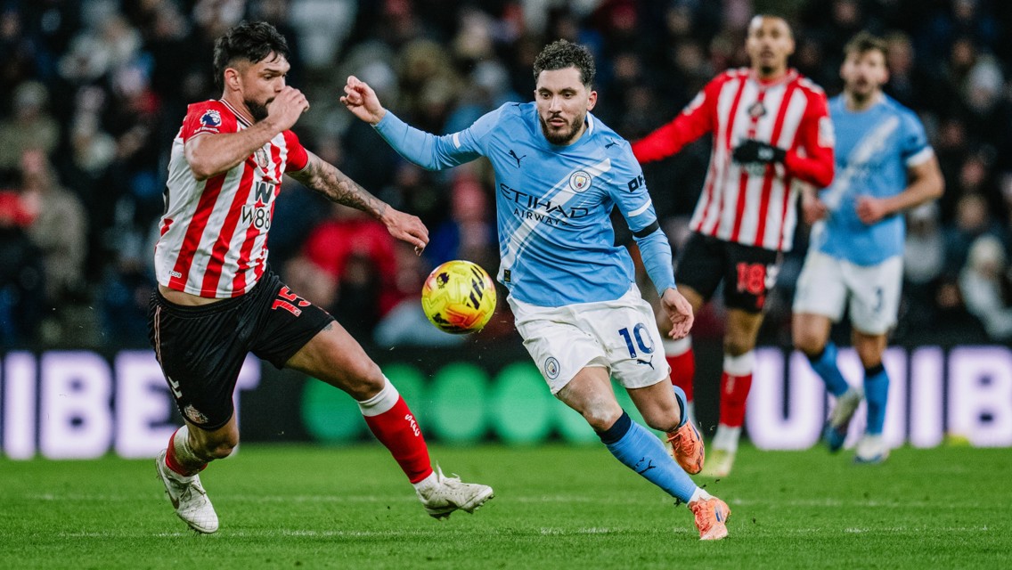 A soccer match scene showing players from Manchester City and Brentford competing for the ball on the field.