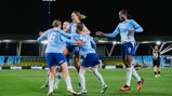 Five Manchester City women football players in light blue jerseys celebrating a goal on the field, with one opposing player visible in the background.