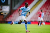 A Manchester City player is in action on the field during a football match. The player is wearing a light blue Manchester City kit and running across the green pitch.