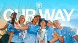 Group of people in Manchester City shirts taking a selfie with a trophy. Text 'OUR WAY' is displayed above with the Manchester City logo.