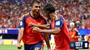 Two Spain football players celebrating during a match with one player pointing towards the other. The crowd is visible in the background. The City at the World Cup and FIFA logos are visible.