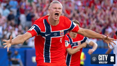 A football player in a red Norway jersey celebrating in a stadium. The jersey has the Norway flag design and the Manchester City logo appears in the corner.