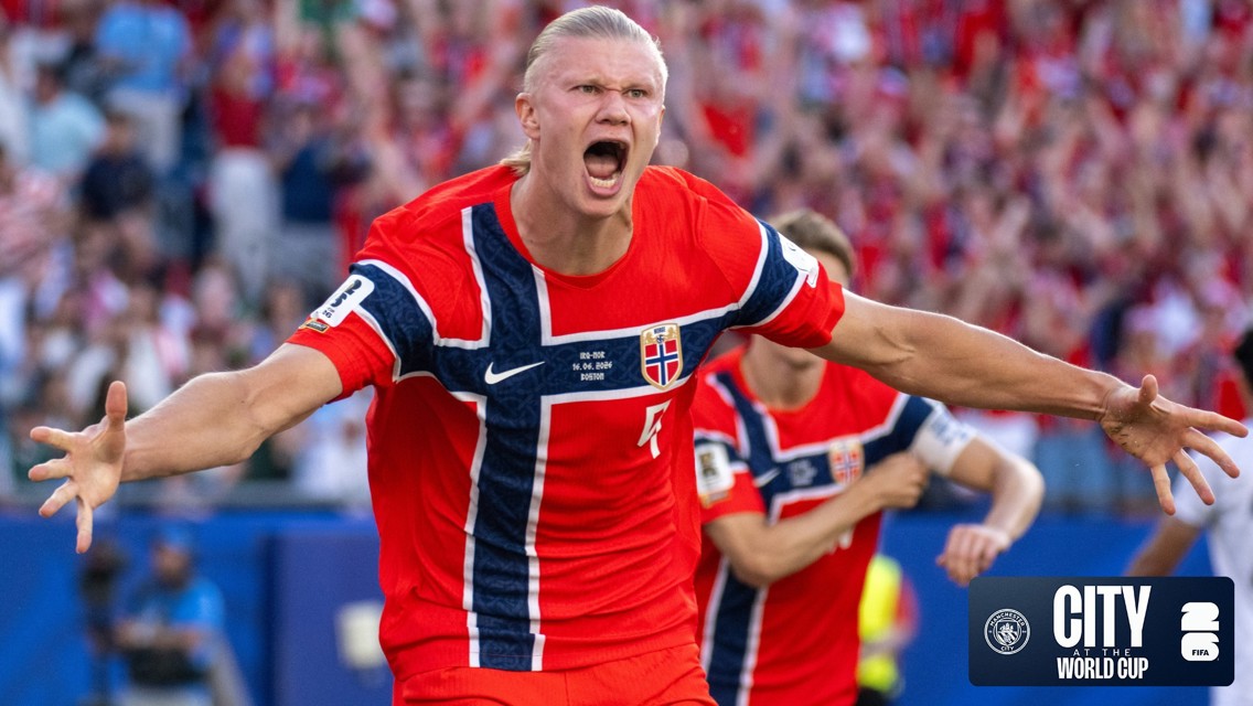 A football player in a red Norway jersey celebrating in a stadium. The jersey has the Norway flag design and the Manchester City logo appears in the corner.