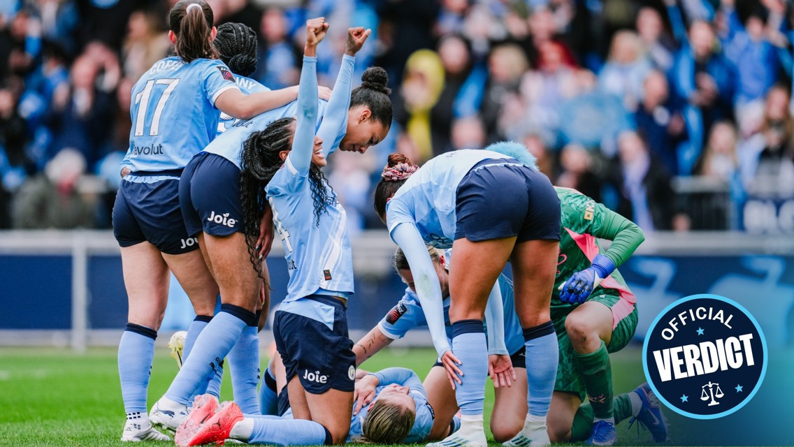 Manchester City women's team players celebrate a goal on the field, with one player lying on the ground. The team's jerseys display sponsors and the team's crest.