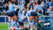 Manchester City women's team players celebrate a goal on the field, with one player lying on the ground. The team's jerseys display sponsors and the team's crest.