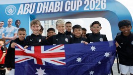 A group of young athletes holding the Australian flag in front of the 'Abu Dhabi Cup 2026' banner.