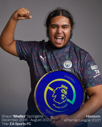 A person wearing a Manchester City esports jersey holds an ePremier League champion plate, celebrating with a raised fist.
