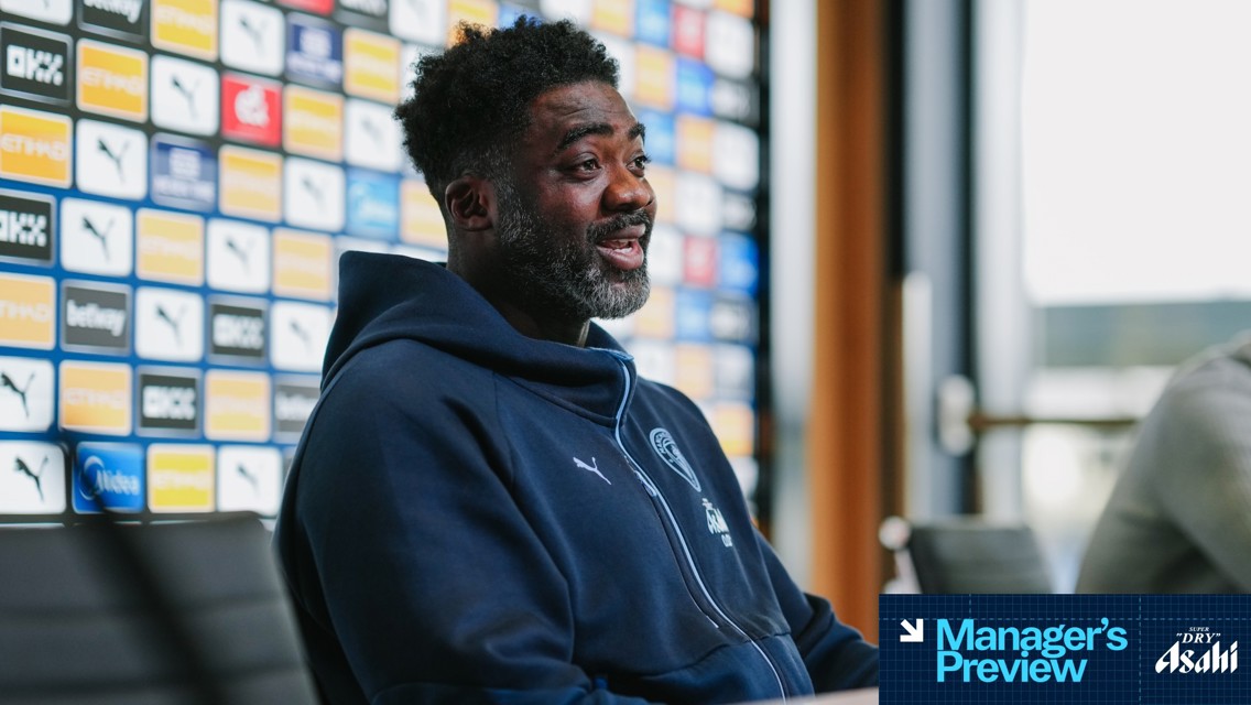 An individual in a Leeds United hoodie participates in a manager's preview session, with a blurred face and sponsorship backdrop behind them.